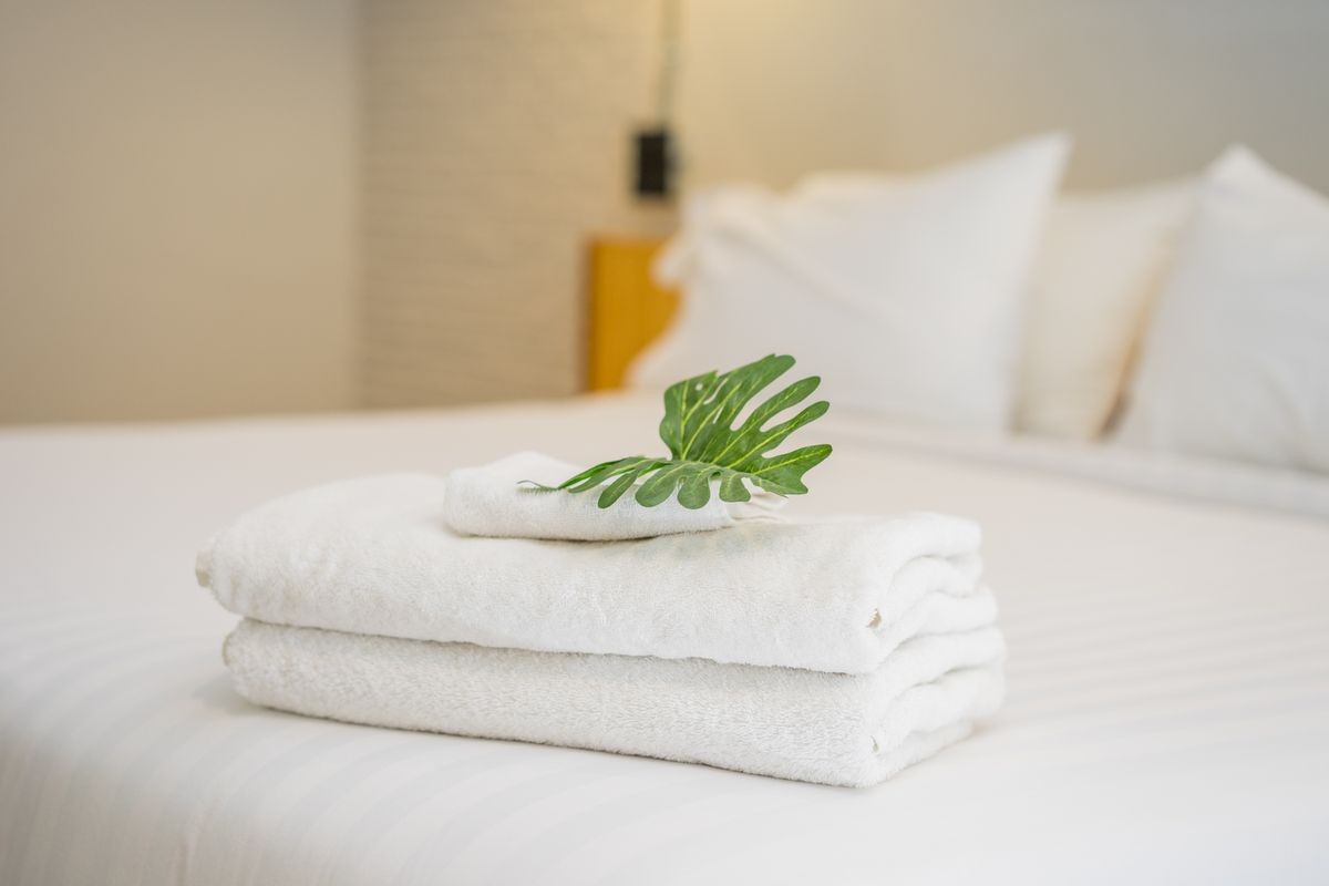Stack of White hotel towel with green leafs on bed decoration in bedroom interior.